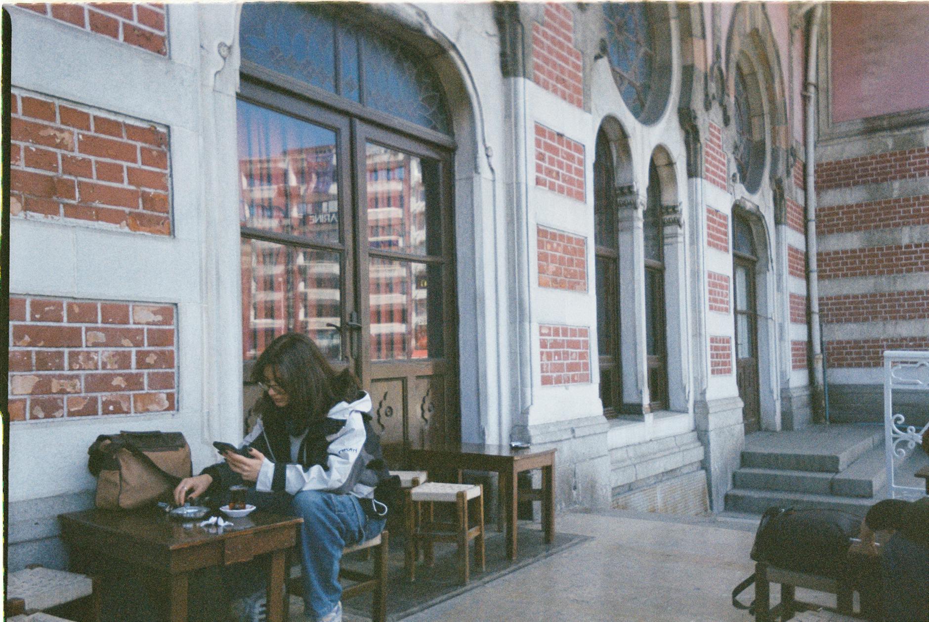 brunette woman sitting at small table by wall and windows